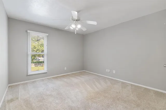 an empty room with a chandelier fan and windows