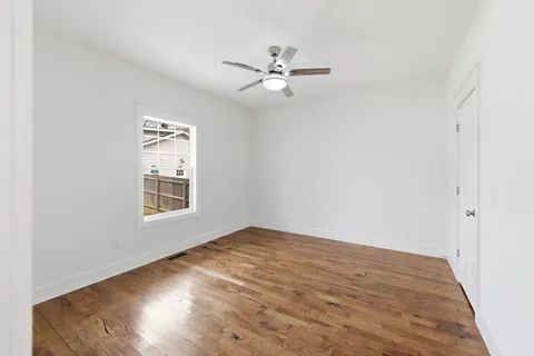an empty room with wooden floor fan and windows
