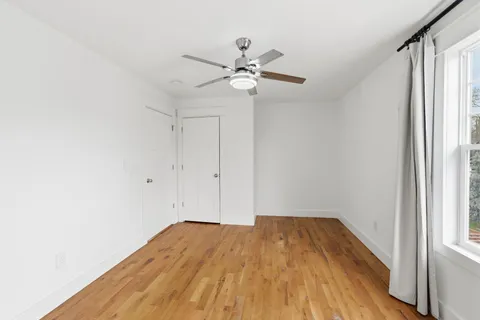 a view of empty room with wooden floor and fan