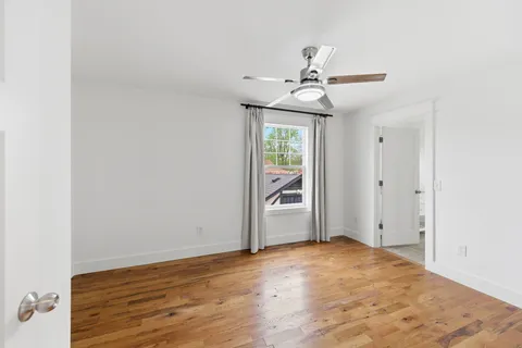 an empty room with wooden floor fan and windows