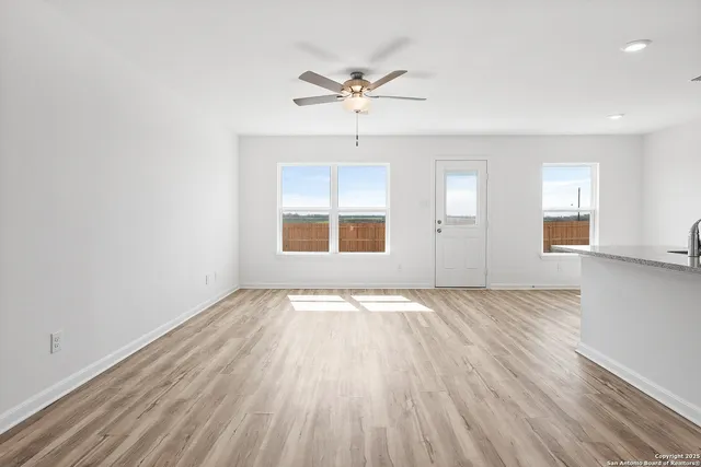 an empty room with wooden floor chandelier fan and windows