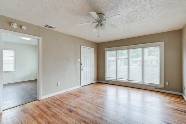 a view of an empty room with a window and wooden floor