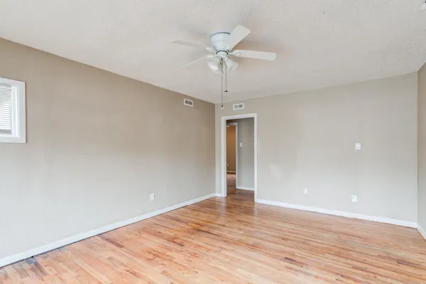 a view of an empty room with wooden floor and a ceiling fan