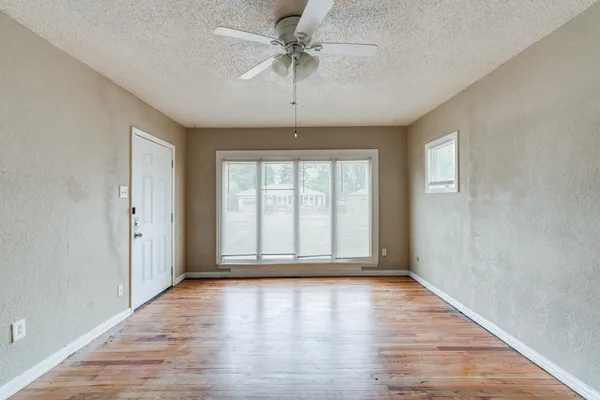an empty room with wooden floor chandelier fan and windows