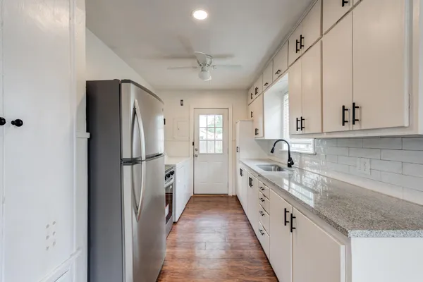 a kitchen with stainless steel appliances granite countertop a refrigerator a sink and white cabinets