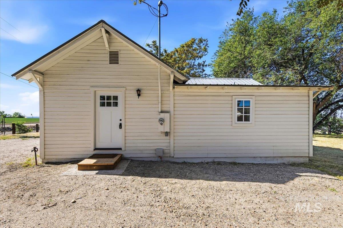 109 Parma Road Parma, ID 83660 - Photo 23 of 31 White horizontal siding exterior with a dark-pitched roof, featuring a white paneled door with glass inserts, an exterior wall lantern, and a single window with white trim