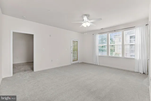 an empty room with chandelier fan and windows