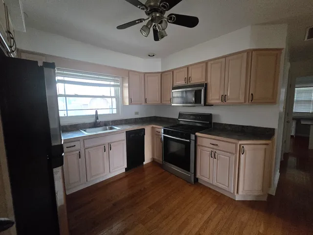 a kitchen with granite countertop stainless steel appliances a sink cabinets and wooden floor