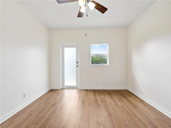 an empty room with wooden floor chandelier fan and windows