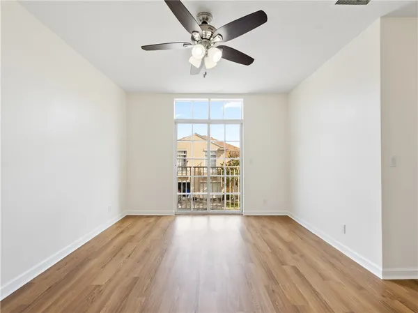 an empty room with wooden floor chandelier fan and windows