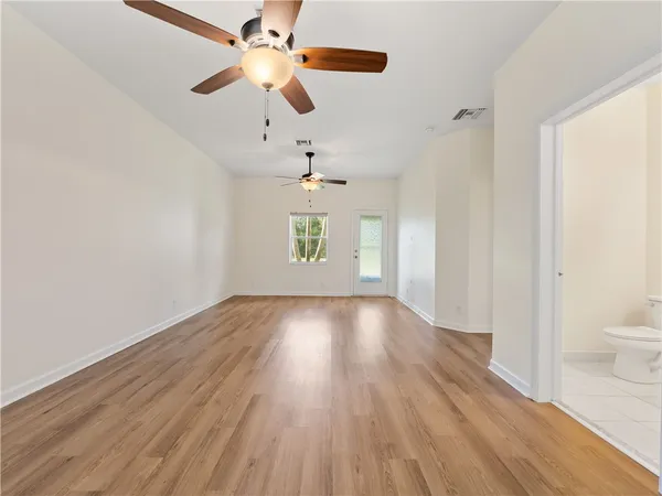 an empty room with wooden floor chandelier fan and windows