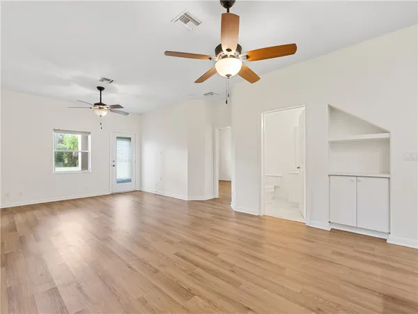 an empty room with wooden floor chandelier fan and windows