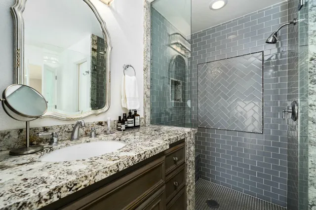a bathroom with a granite countertop sink a mirror and shower