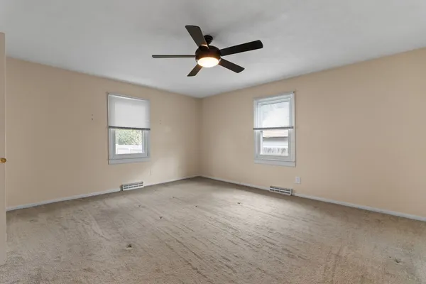 an empty room with ceiling fan and windows