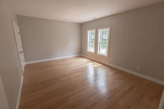a view of an empty room with wooden floor and window