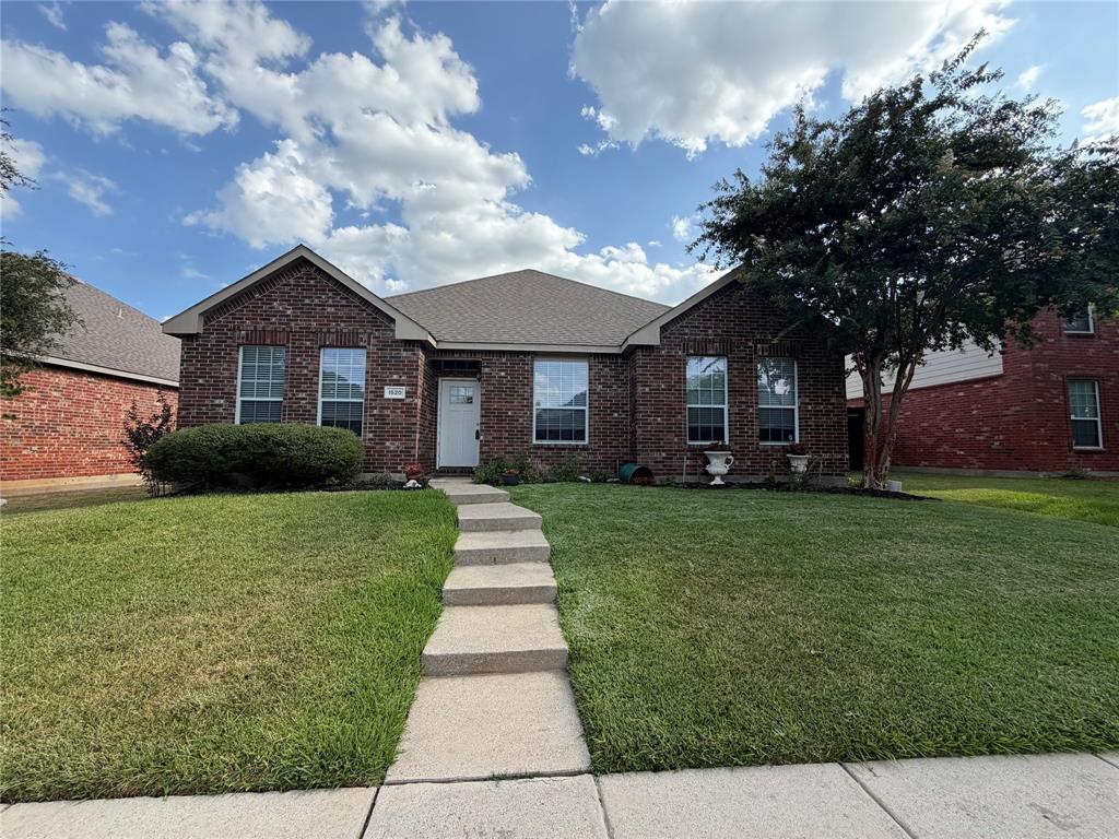 Brick exterior with a gabled roofline, concrete walkway, established front lawn, and mature trees