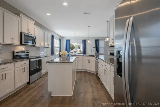 a kitchen with stainless steel appliances granite countertop a refrigerator a sink dishwasher a stove and white cabinets with wooden floor