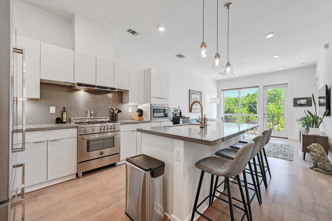 a kitchen with stainless steel appliances granite countertop white cabinets a sink a stove a dining table and chairs