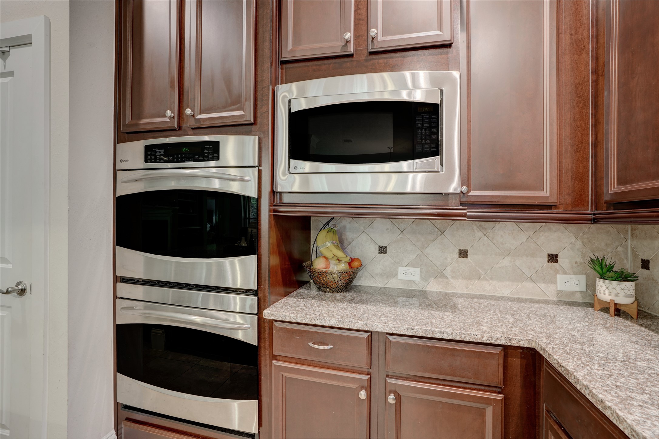 27243 Jessica Hills Lane Spring, TX 77386 - Photo 14 of 49 This kitchen features elegant dark wood cabinetry with stainless steel appliances, including a built-in microwave and double oven. The granite countertops and tile backsplash add a touch of sophistication, making it a perfect space for culinary enthusiasts.