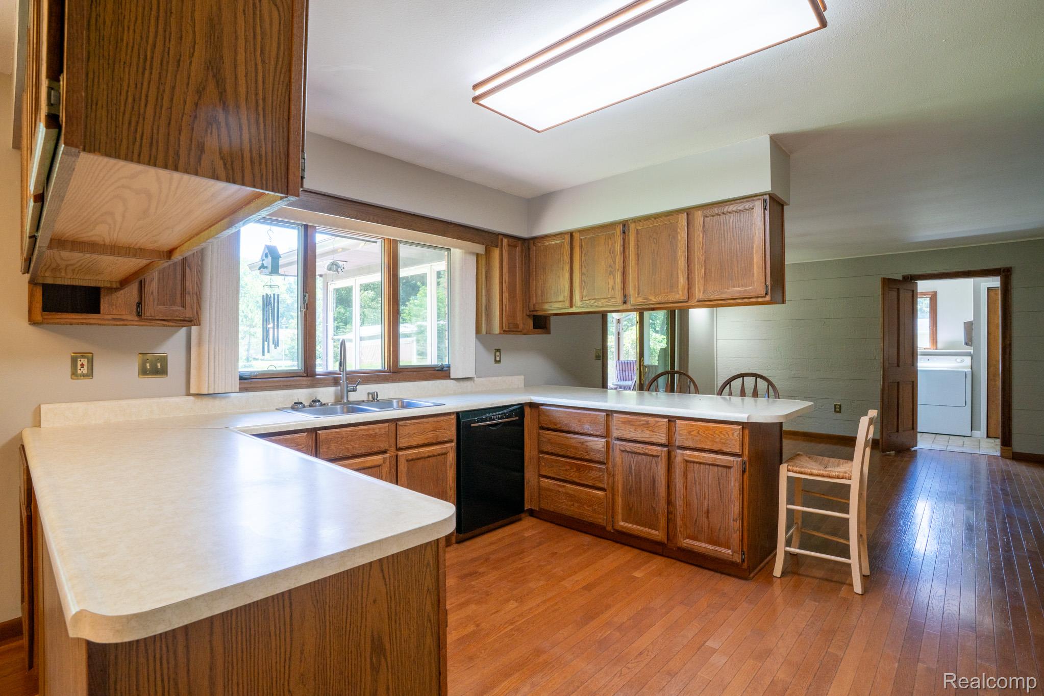 12900 Maxwell Road Carleton, MI 48117 - Photo 32 of 59 Hardwood flooring, wood-finish cabinetry, built-in dishwasher, stainless steel sink, and a large window above the sink