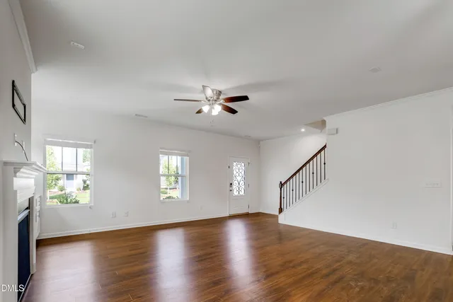 an empty room with wooden floor a ceiling fan a fireplace and windows