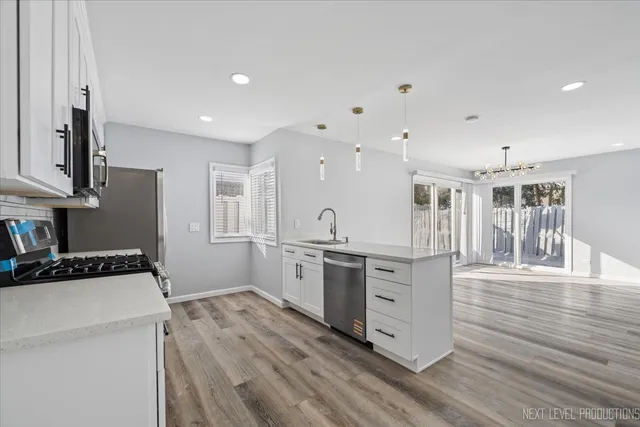 a kitchen with stainless steel appliances a stove top oven a sink a refrigerator white cabinets and wooden floor