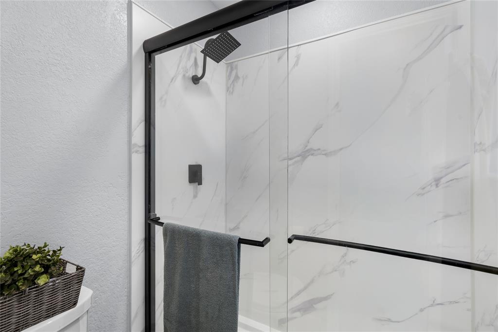 7629 Cedarhill Road Watauga, TX 76148 - Photo 19 of 26 Shower enclosure with black-framed glass door, white marble-patterned shower walls, and a matte black rainfall showerhead