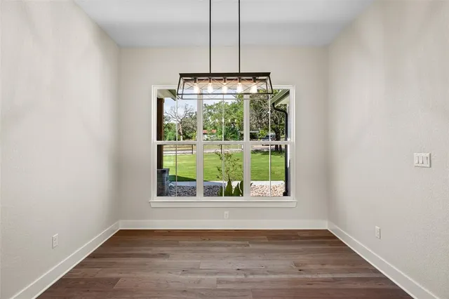 a view of an empty room with wooden floor kitchen view and a window