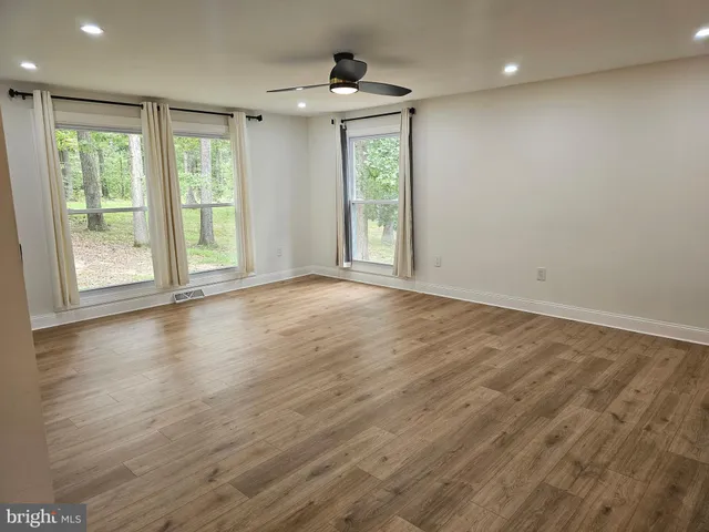 an empty room with wooden floor fan and windows