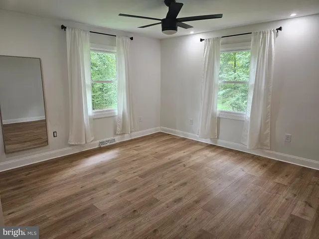 an empty room with wooden floor fan and windows