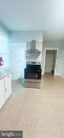 a living room with stainless steel appliances kitchen island a stove a refrigerator and white cabinets with wooden floor