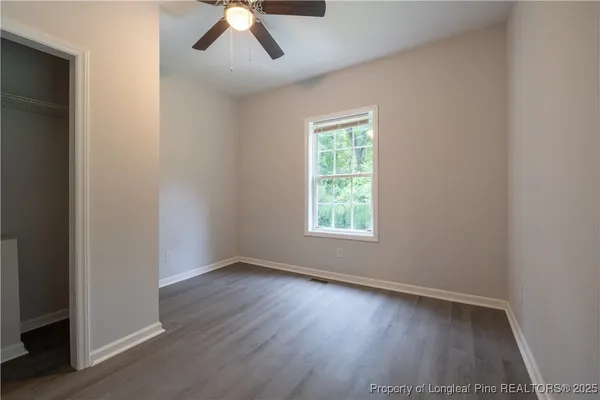 an empty room with wooden floor chandelier fan and windows