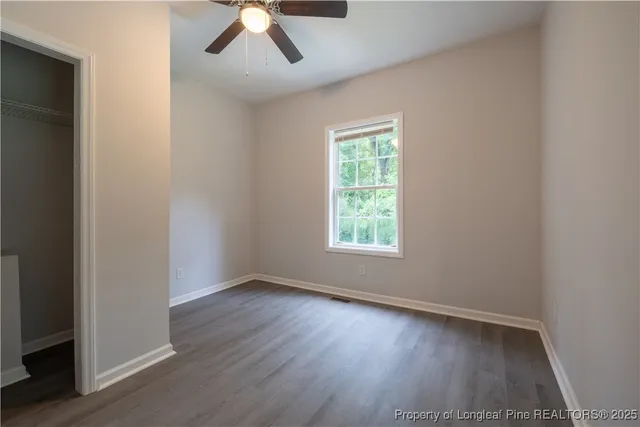 an empty room with wooden floor chandelier fan and windows
