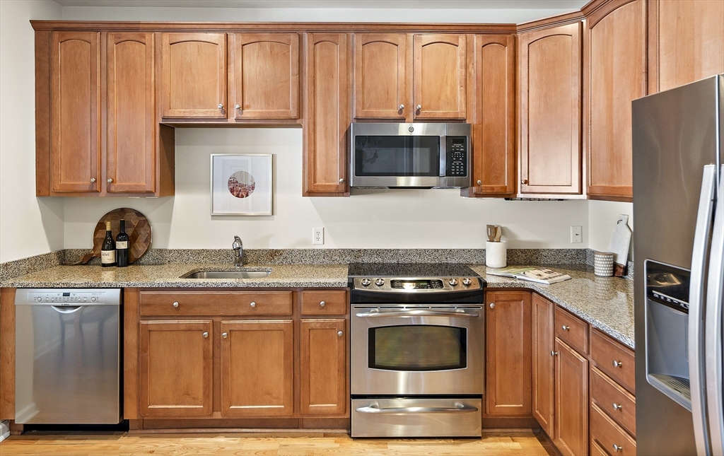 107 Clocktower Drive, Unit 303 Waltham, MA 02452 - Photo 6 of 18 a kitchen with granite countertop a stove top oven microwave and refrigerator