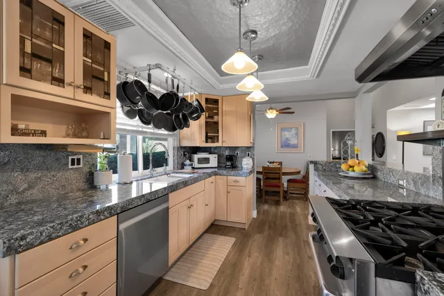 a kitchen with stainless steel appliances granite countertop a stove a sink dishwasher a dining table and chairs with wooden floor