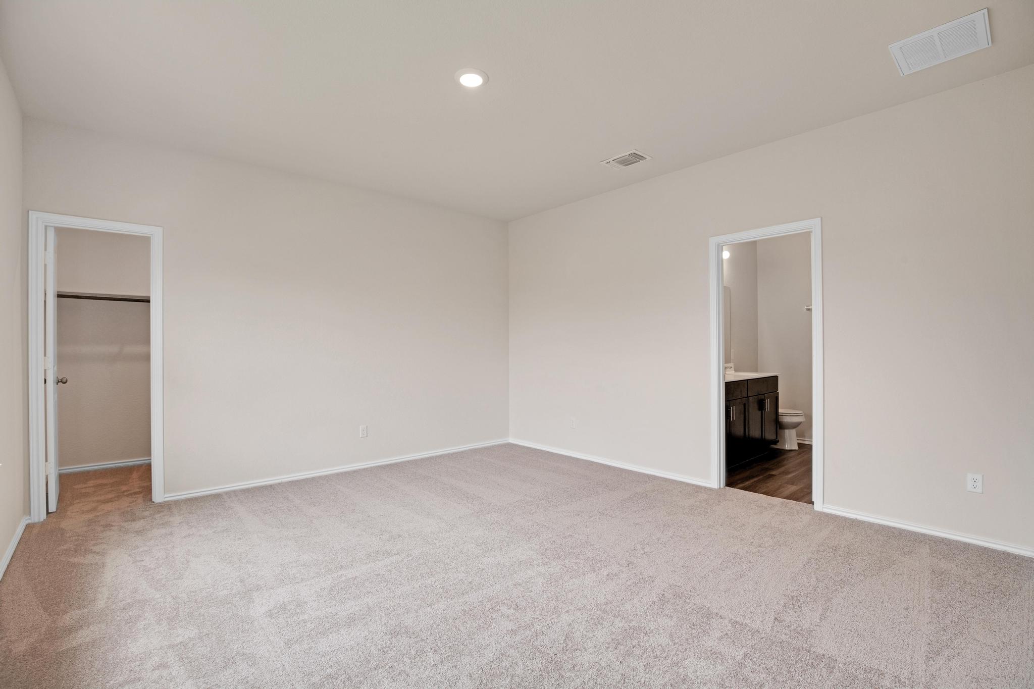 200 Janice Road Taylor, TX 76574 - Photo 9 of 25 A spacious bedroom with plush carpeting leads to a walk-in closet and an en-suite bathroom.