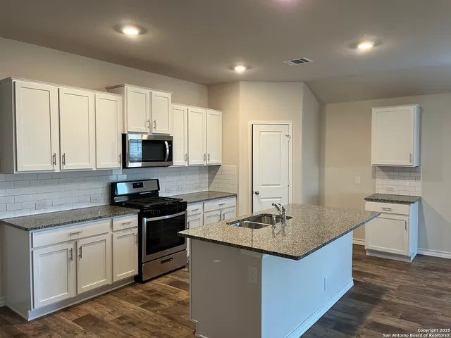 a kitchen with kitchen island granite countertop white cabinets sink and stainless steel appliances