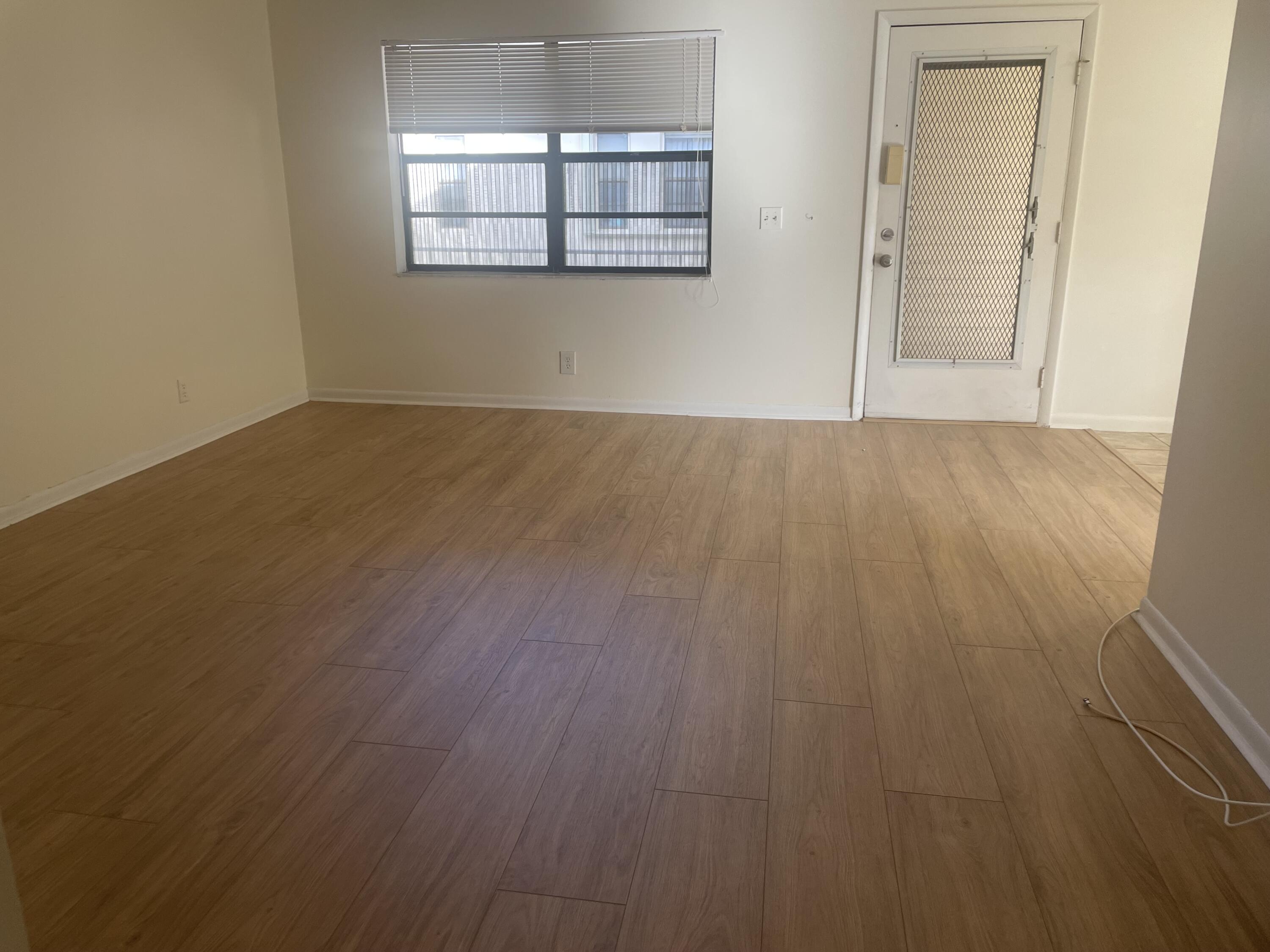 83 Capri B, Unit B Delray Beach, FL 33484 - Photo 5 of 26 an empty room with wooden floor white walls and windows