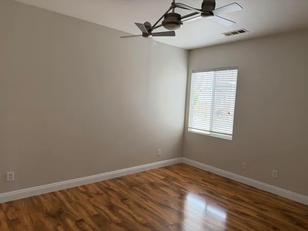 an empty room with wooden floor ceiling fan and windows