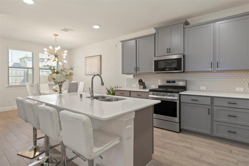 4125 Fern Loop Forney, TX 75126 - Photo 8 of 40 Kitchen featuring an island with a built-in sink, gray cabinetry, white countertops, stainless steel appliances, and a white hexagonal tile backsplash