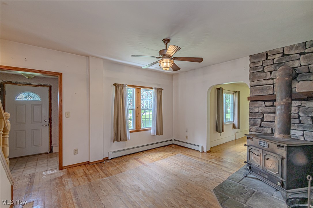 749 Hartman Road Wadsworth, OH 44281 - Photo 23 of 49 Unfurnished living room with ceiling fan, light hardwood / wood-style flooring, a wood stove, and a healthy amount of sunlight