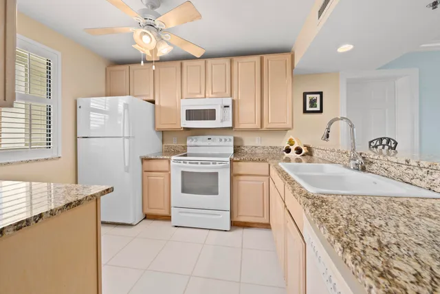 a kitchen with granite countertop a sink stove a refrigerator and white cabinets with wooden floor