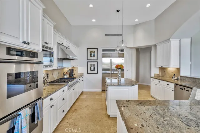 a large kitchen with stainless steel appliances kitchen island granite countertop a refrigerator oven a sink dishwasher and white cabinets with wooden floor