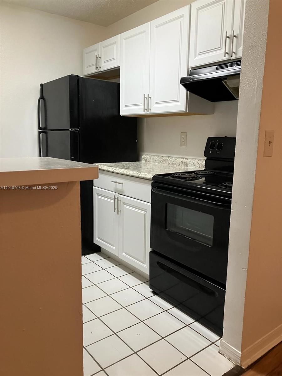 4025 West McNab Road, Unit E105 Pompano Beach, FL 33069 - Photo 4 of 9 a kitchen with granite countertop white cabinets and black appliances