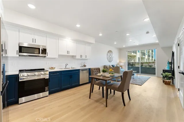 a kitchen with stainless steel appliances kitchen island granite countertop a stove a sink a microwave a dining table and chairs with wooden floor
