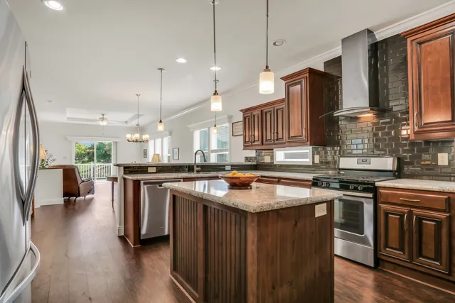 a kitchen with stainless steel appliances granite countertop a stove a sink dishwasher a refrigerator and a dining table with wooden floor