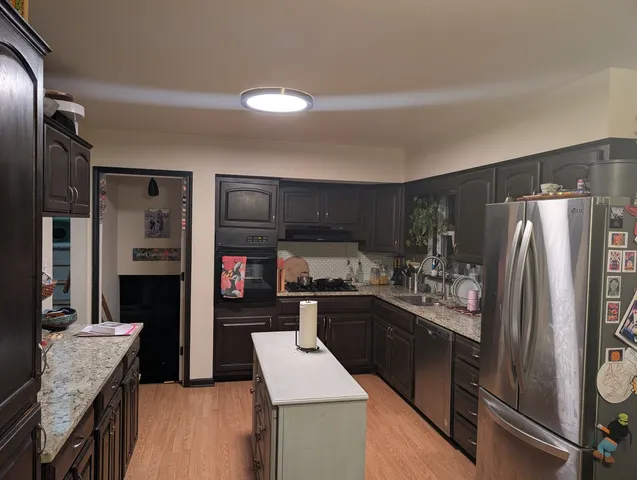 a kitchen with stainless steel appliances kitchen island granite countertop a refrigerator a stove and a sink with wooden floor