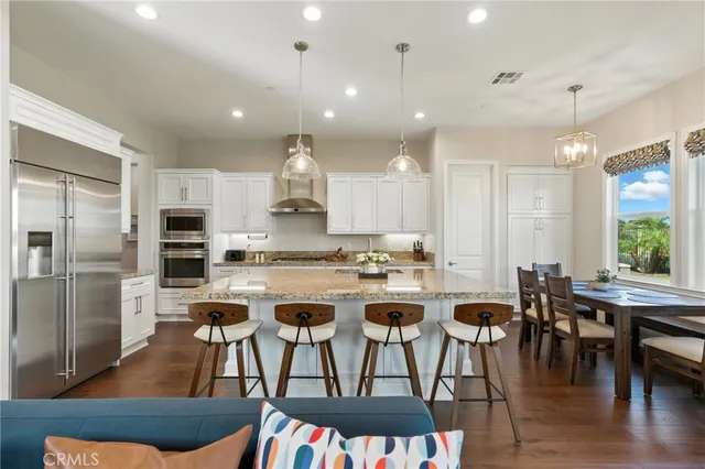 a kitchen with stainless steel appliances kitchen island granite countertop a dining table chairs refrigerator and sink