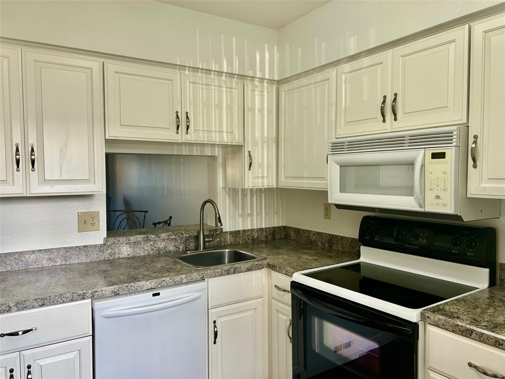 1701 Pinehurst Road, Unit 18C Dunedin, FL 34698 - Photo 4 of 17 a kitchen with granite countertop white cabinets and black appliances
