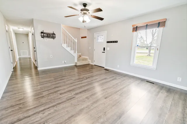 a view of an empty room with wooden floor and a ceiling fan